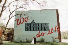 bride and groom pose in front of a detroit mural by wedding photographer heather jowett