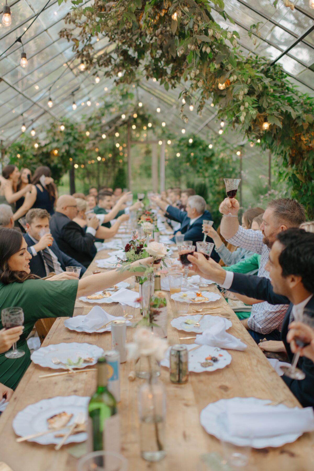 wedding guests toasting glasses during a reception in a greenhouse.