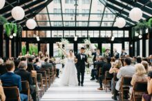 The bride and groom recess joyfully back down the aisle as newlyweds hands raised in celebration while guests cheer from their seats