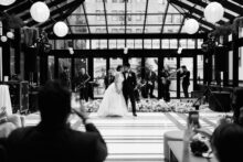 The couple shares their first dance beneath a glass atrium with live band playing in the background at their Shinola Hotel wedding reception