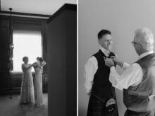 The brides mother fastens the back of her gown in front of a tall window while the groom gets help adjusting his tie from his father