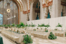 Elegant wedding reception setup by Simply Brilliant Events at the Guardian Building in Detroit featuring long tables with tropical greenery centerpieces