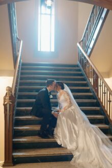 Cinematic moment between bride and groom framed by gothic windows and iron railings on the grand staircase of their Detroit Masonic Temple wedding
