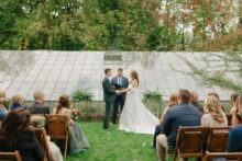 Bride and groom laugh while reading vows during ceremony at Glass House Community