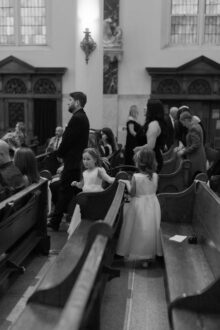 Black and white candid photo of flower girls holding hands and walking down the aisle inside Saints Peter and Paul Jesuit Church in Detroit captured in fine art documentary style