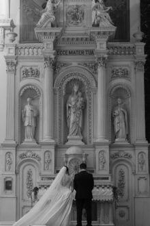 Bride and groom praying before a religious altar at Saints Peter and Paul Jesuit Church in Detroit surrounded by ornate Catholic architecture in a timeless black and white wedding portrait