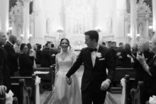Black and white image of bride and groom walking hand in hand up the aisle after their wedding ceremony at Saints Peter and Paul Jesuit Church