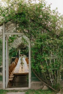 View through greenhouse doorway framing a long table set for a romantic fall wedding dinner