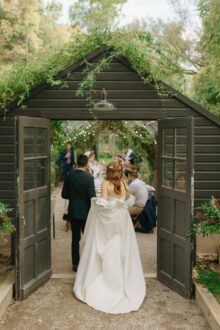 The bride and groom walk hand in hand into their candlelit greenhouse reception at Glass House Community