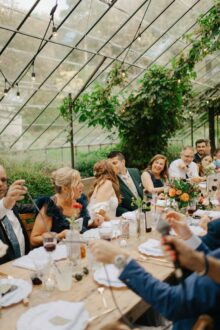 The newlyweds share a kiss during their reception at glass house community surrounded by joyful guests