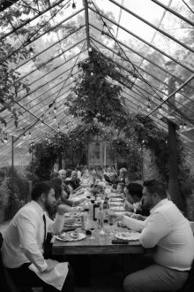 wedding guests dining at a long table inside the greenhouse at Glass House Community