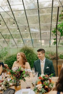 bride and groom laughing together as a toast draws smiles from guests at their greenhouse dinner table