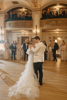 Bride and groom share a joyful first dance surrounded by guests beneath gilded balconies and chandeliers inside the Detroit Masonic Temple Crystal Ballroom