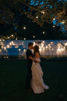 bride and groom embracing in front of the greenhouse at Glass House Community at night
