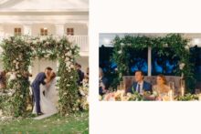 Bride and groom have a first kiss amongst a lush floral arch.