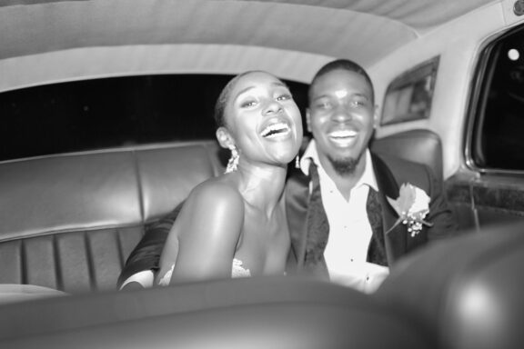 Bride and groom laughing in the back of their classic getaway car.