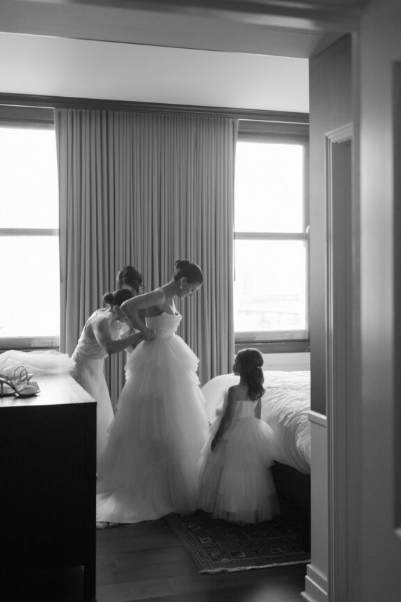 A bride getting into her dress in a suite at the David Whitney building, helped by her mother, sister, and flower girl.