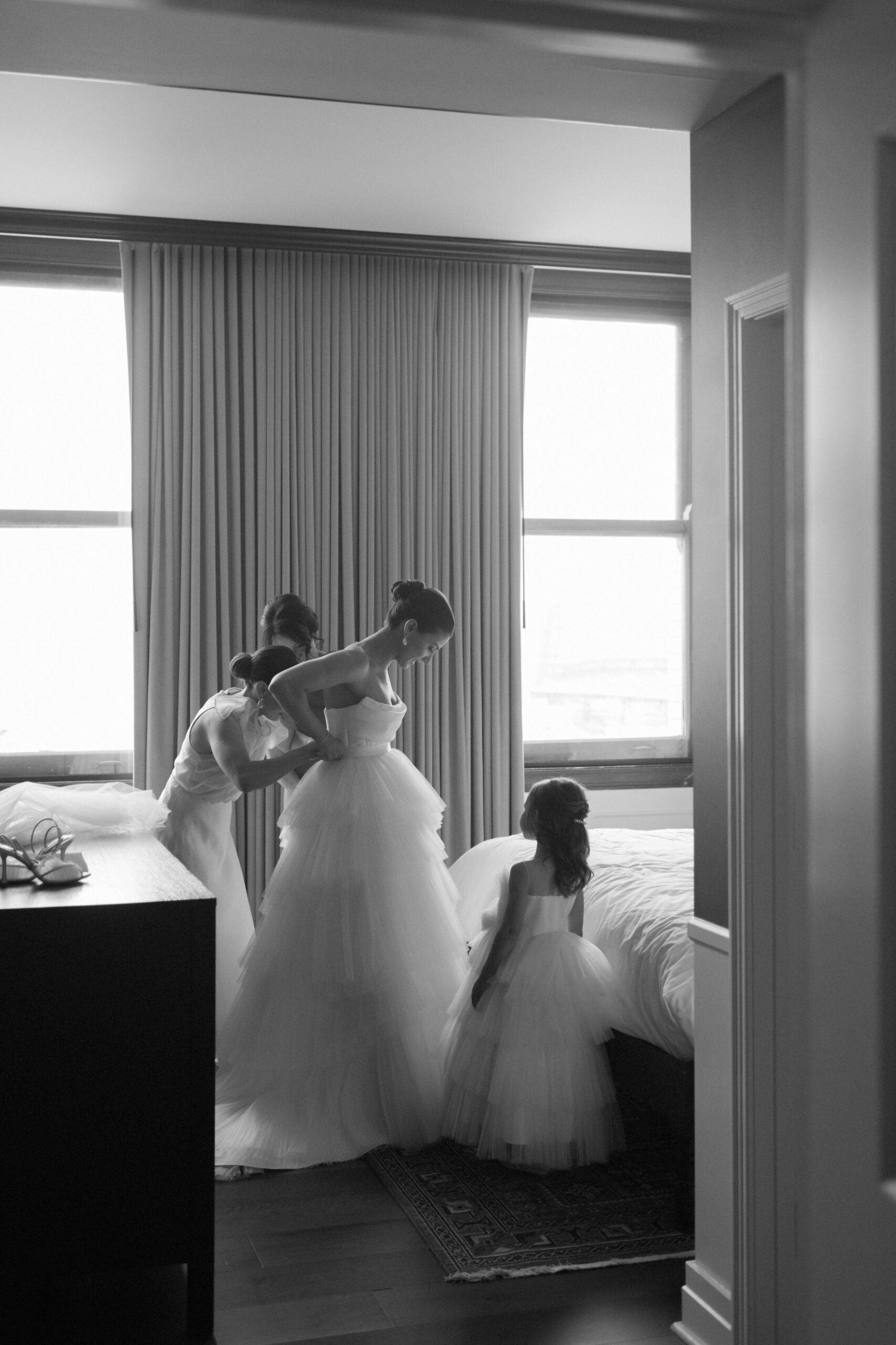 A bride getting into her dress in a suite at the David Whitney building, helped by her mother, sister, and flower girl.