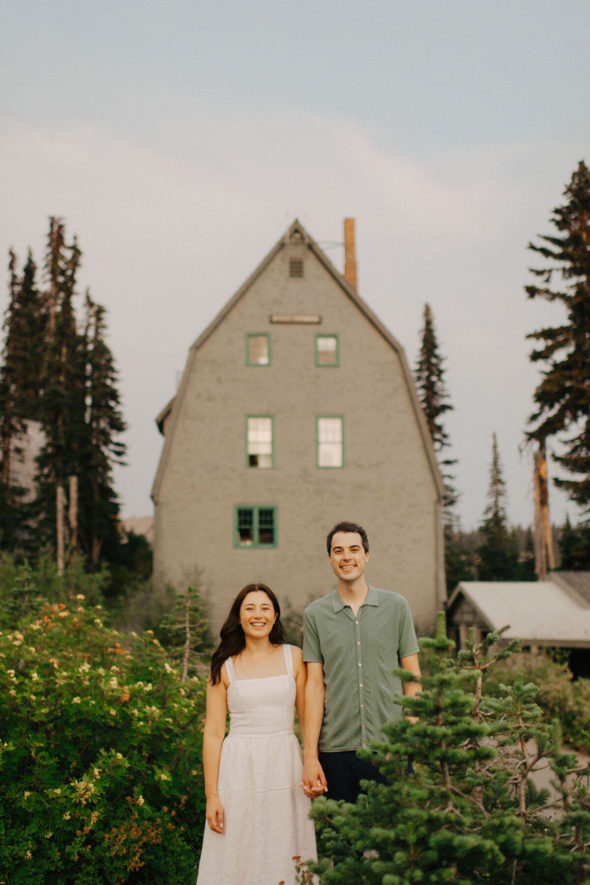 A couple poses in front of a building at mount rainier national park during their engagement session.